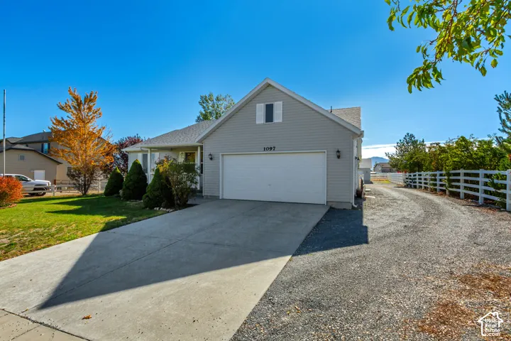 Gray siding exterior with a white garage door, concrete driveway, and gravel side drive