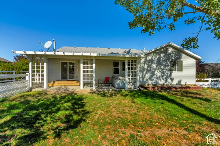 Rear exterior with light gray siding, white lattice pergola, white privacy fencing, and wood steps leading to a sliding glass door
