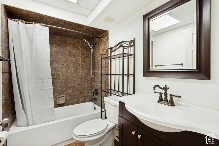 Bathtub with tiled surround, dark wood-finish vanity with an integrated sink, framed mirror, and bronze-finish fixtures