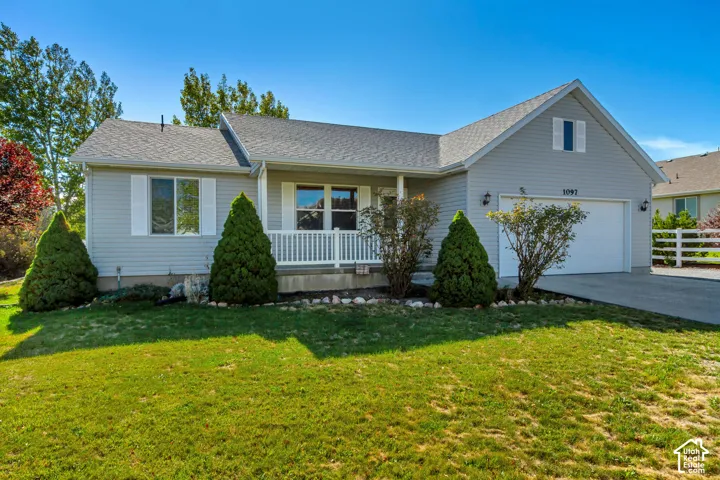 Siding exterior featuring a covered porch with white railing, attached garage, and mature landscaping
