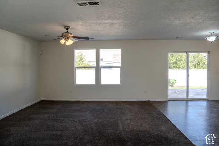 Spacious interior with neutral wall paint, two windows, a ceiling fan, and a sliding glass door