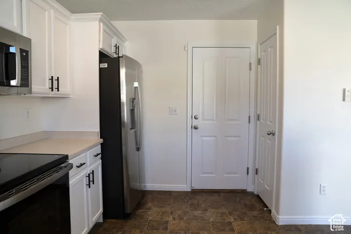 Stainless steel appliances, white cabinetry with crown molding, light-toned countertops, and a tiled floor