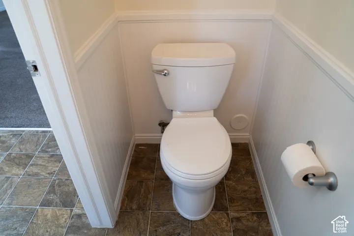 White toilet with a chrome flush lever, wainscoting, and tile flooring