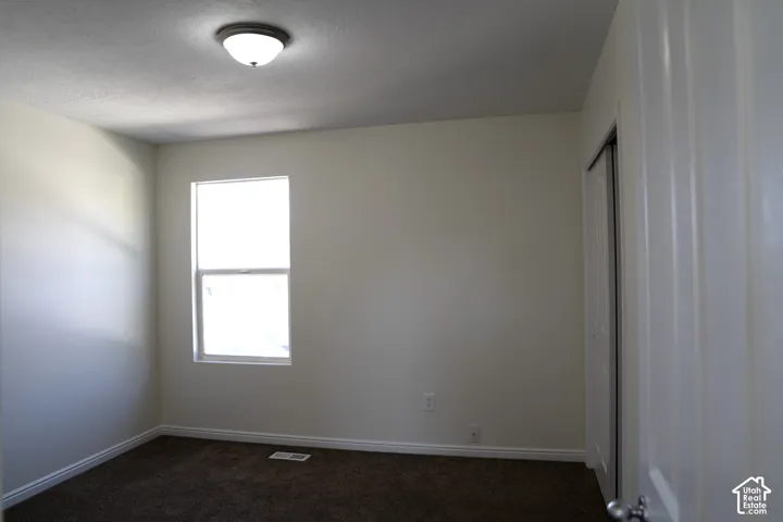 Neutral wall color, carpeted flooring, single window, flush-mount ceiling light fixture, and a closet with bifold doors