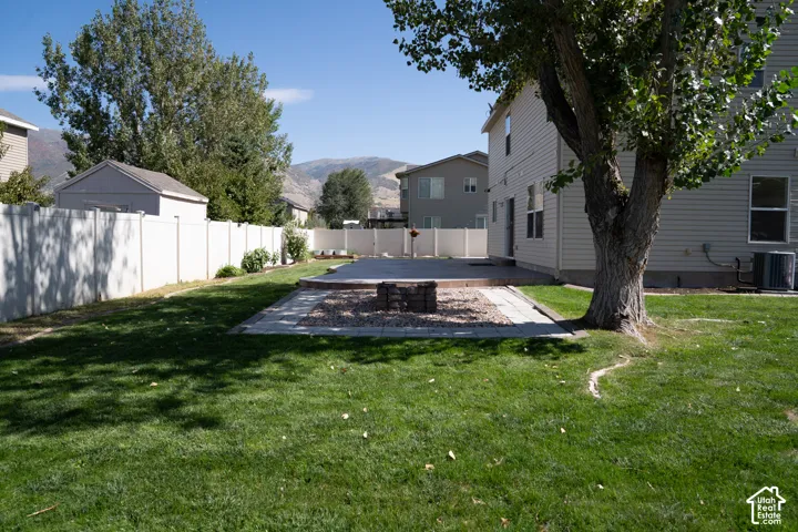 Expansive lawn area, concrete patio, built-in fire pit with stone surround, full fencing, and a mature shade tree