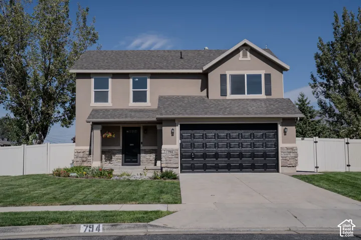 Stucco exterior with stone accents, attached garage, covered front porch, and a white fence
