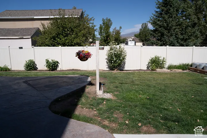 Expansive backyard featuring a manicured lawn, white privacy fencing, and mature trees