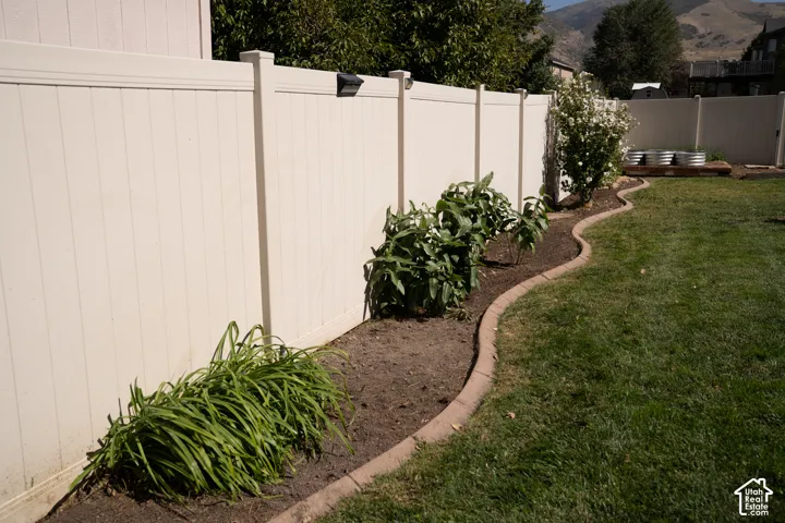 Well-manicured backyard featuring a mature landscaped perimeter with established greenery, vinyl privacy fencing, curved hardscape edging, and lush lawn space ideal for outdoor enjoyment