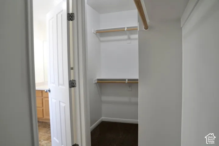 Walk-in closet featuring dual wood-finish shelving rods, multiple storage shelves, and dark hardwood flooring with abundant natural light from the adjacent room