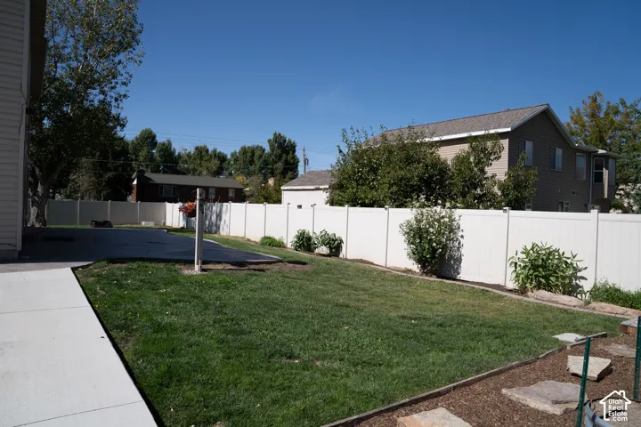 Expansive backyard featuring a manicured lawn, established landscaping, a concrete patio, a concrete pathway, and privacy fencing