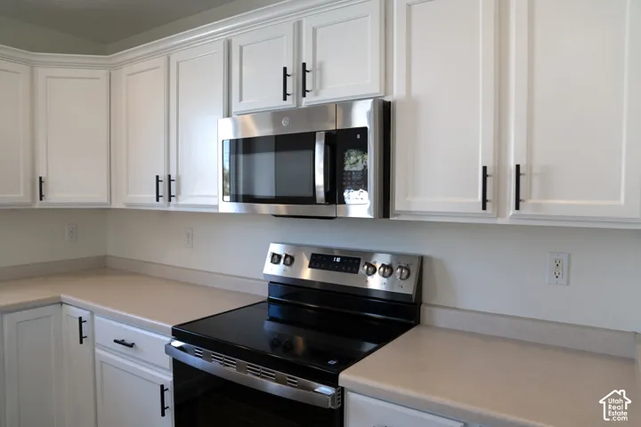 White shaker-style cabinetry with matte black hardware, stainless steel range, and stainless steel microwave