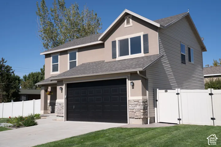 Stucco and siding exterior with stone accents, attached garage, and a white privacy fence