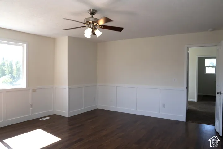 Spacious room with wainscoting detail along lower walls, dark wood-finish flooring, and ceiling fan with integrated lighting