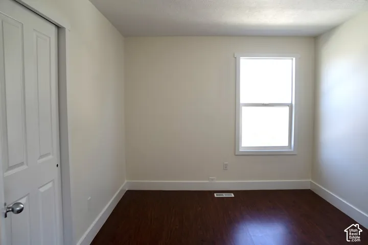 Bright bedroom with hardwood flooring, large window with natural light, six-panel closet door, and neutral wall finishes throughout
