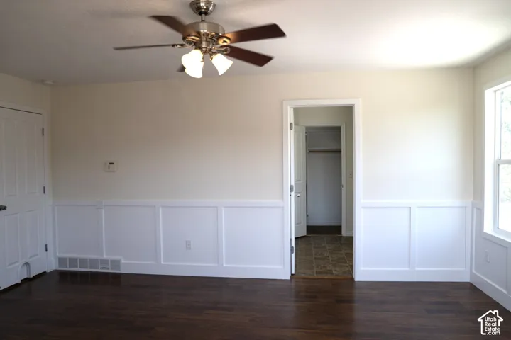 Wood-finish flooring, wainscoting, ceiling fan with light fixture, and an interior door