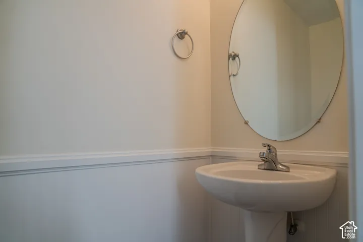 Pedestal sink with a chrome faucet, oval mirror, and wainscoting