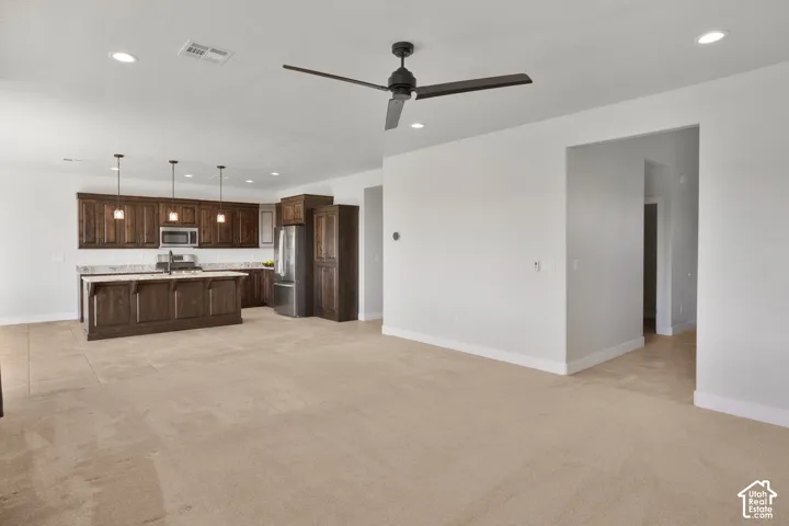 Kitchen island with integrated sink, stainless steel appliances, dark wood cabinetry, and recessed lighting