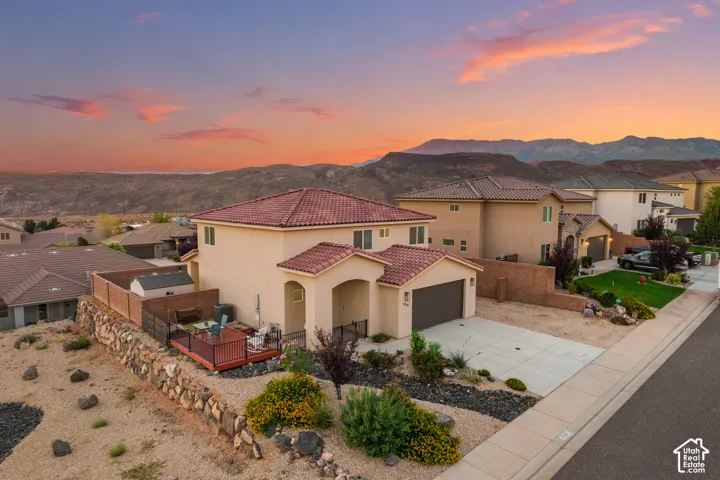 Stucco exterior with a tile roof, paved driveway, attached garage, and a rear deck