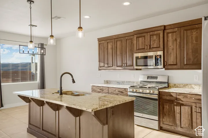 Kitchen featuring rich wood cabinetry, stainless steel appliances, a center island with sink, and pendant lighting
