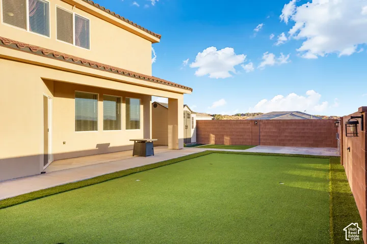 Expansive backyard featuring a putting green, a covered patio, and privacy fencing with attached sconces