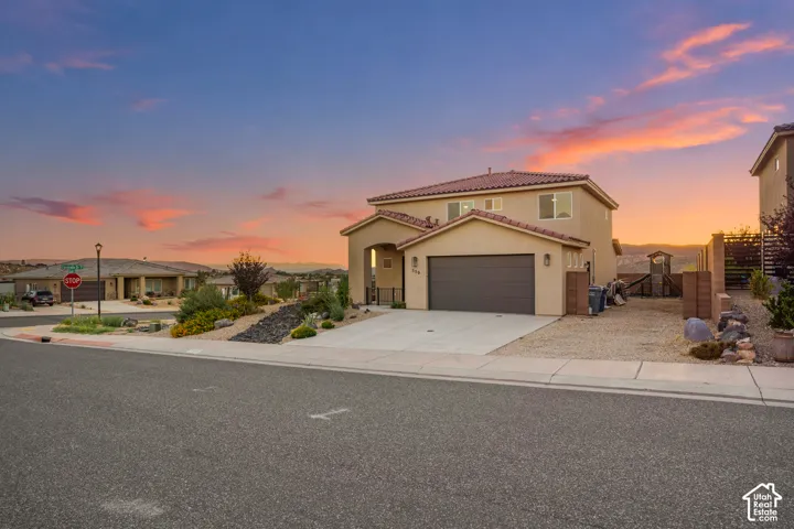 Stucco exterior featuring a tile roof, an integrated garage, a concrete driveway, and low-maintenance landscaping
