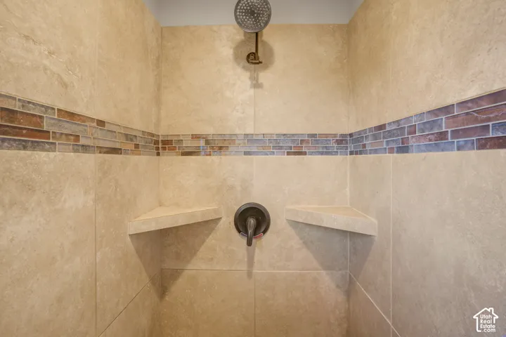 Tiled shower with a mosaic accent band, integrated corner shelves, and a dark-finish shower head and controls