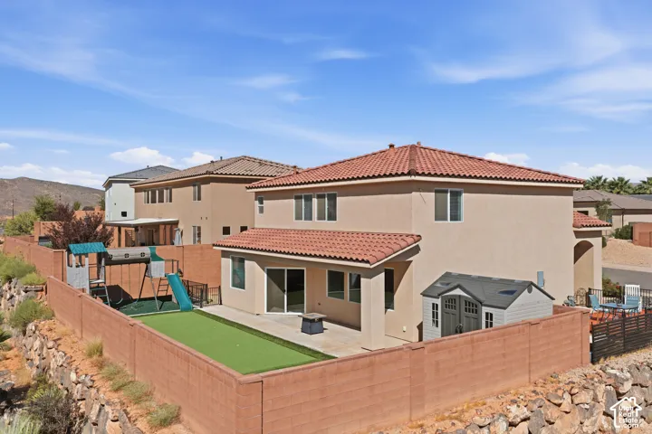 Stucco exterior with a red tile roof, covered patio, sliding glass door, and fenced backyard with artificial turf