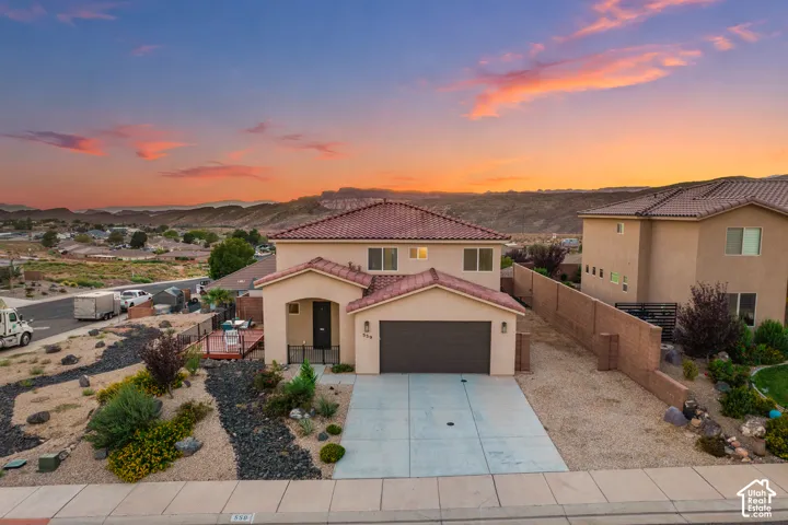 Two-story stucco exterior with a tile roof, an integrated garage, a concrete driveway, and xeriscaping