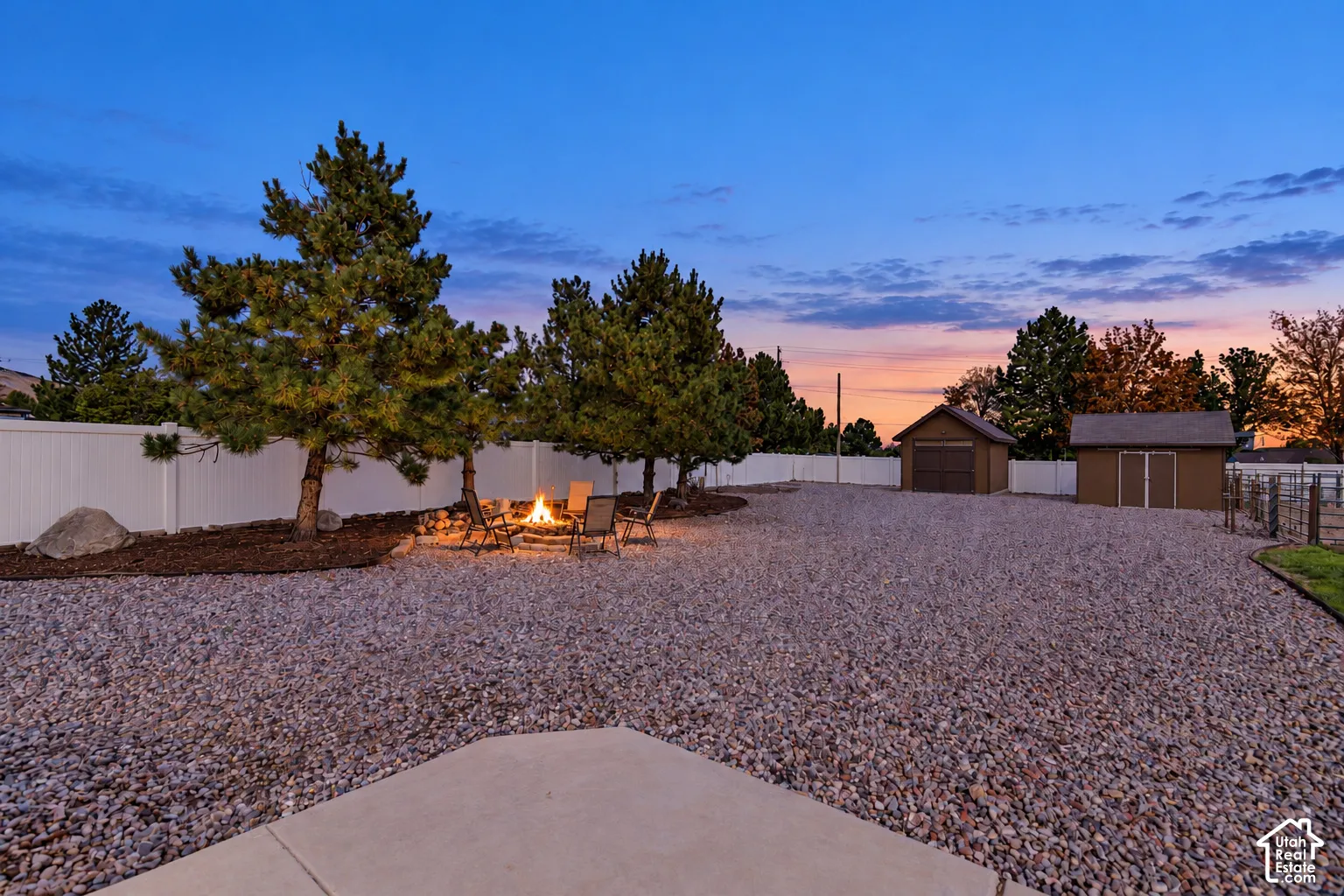 Expansive gravel yard with a concrete patio, white privacy fence, and a stone-lined fire pit area