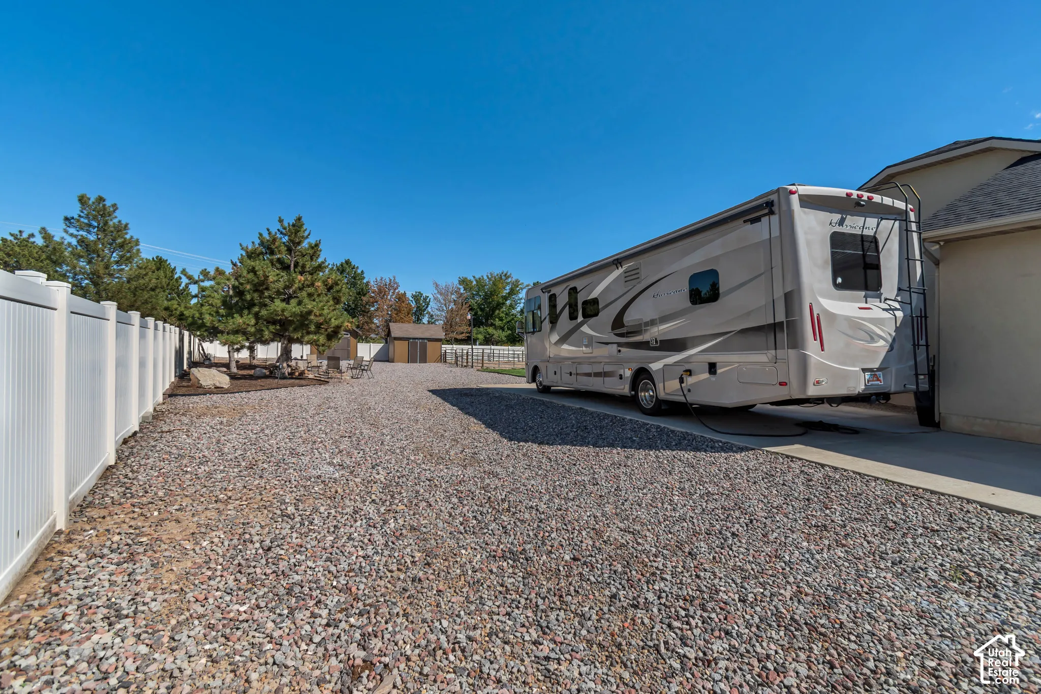 Expansive gravel parking area, white privacy fencing, and a separate storage shed