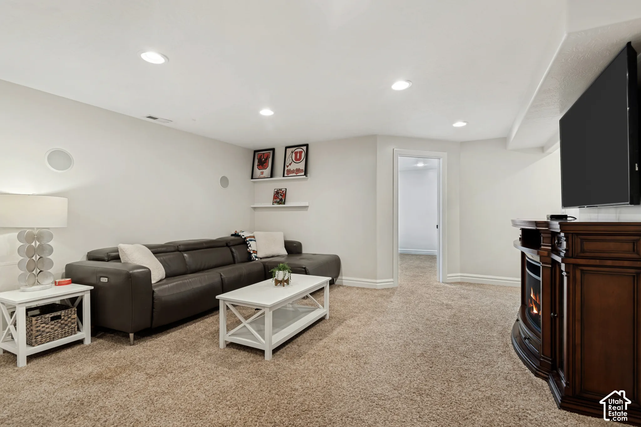 Recessed lighting, light-colored carpeting, built-in shelving, and a dark wood-finish media console with an integrated fireplace