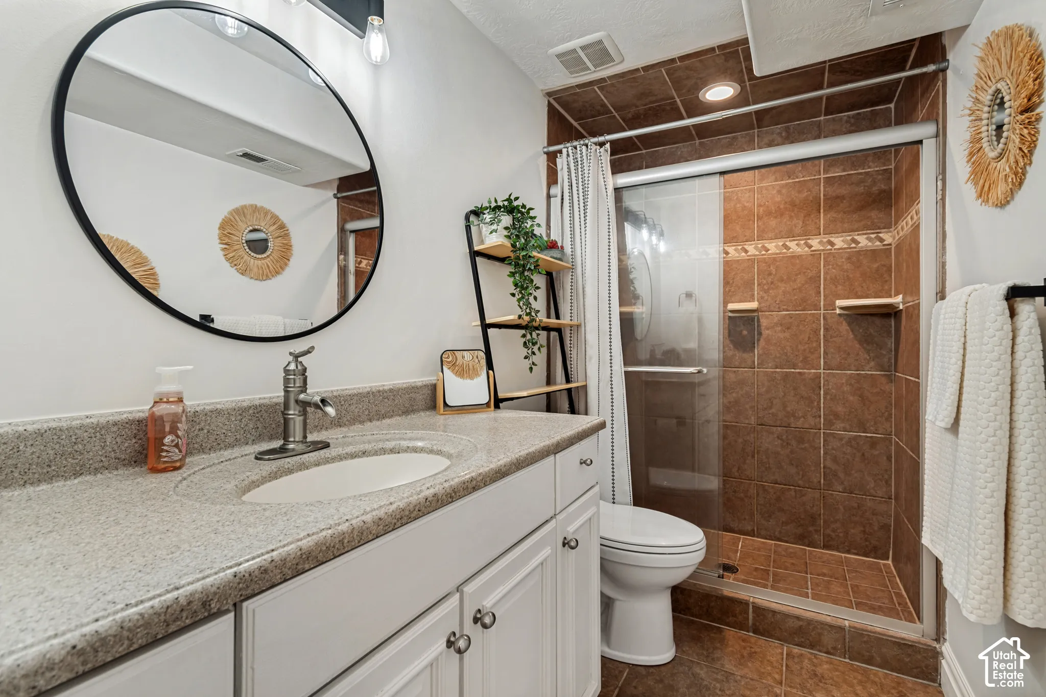 Bathroom featuring a brown tiled shower with a glass enclosure, a white vanity with an integrated sink, and a light-colored countertop