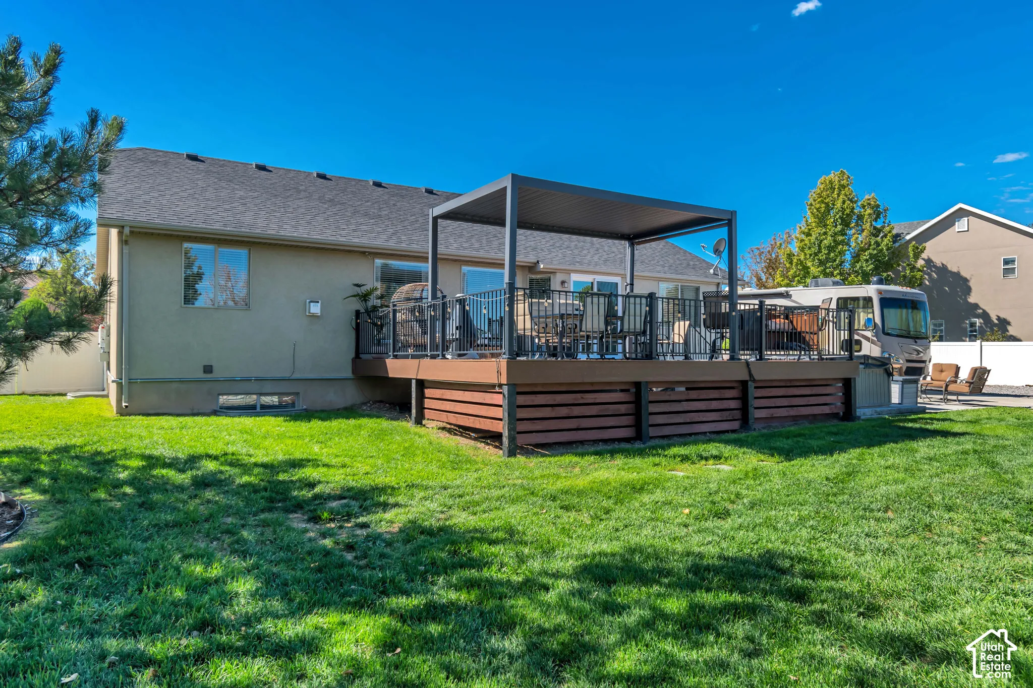 Expansive backyard featuring a large elevated deck with a pergola, black metal railings, and privacy screening