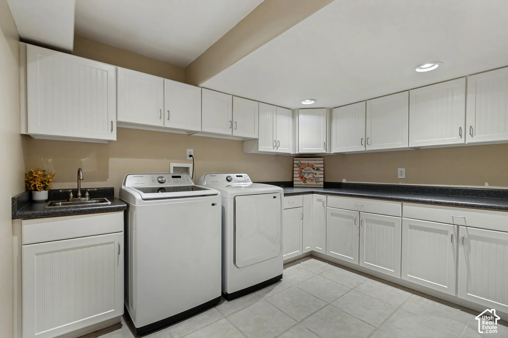 Functional laundry area featuring white cabinetry, dark countertops, a utility sink, and recessed lighting