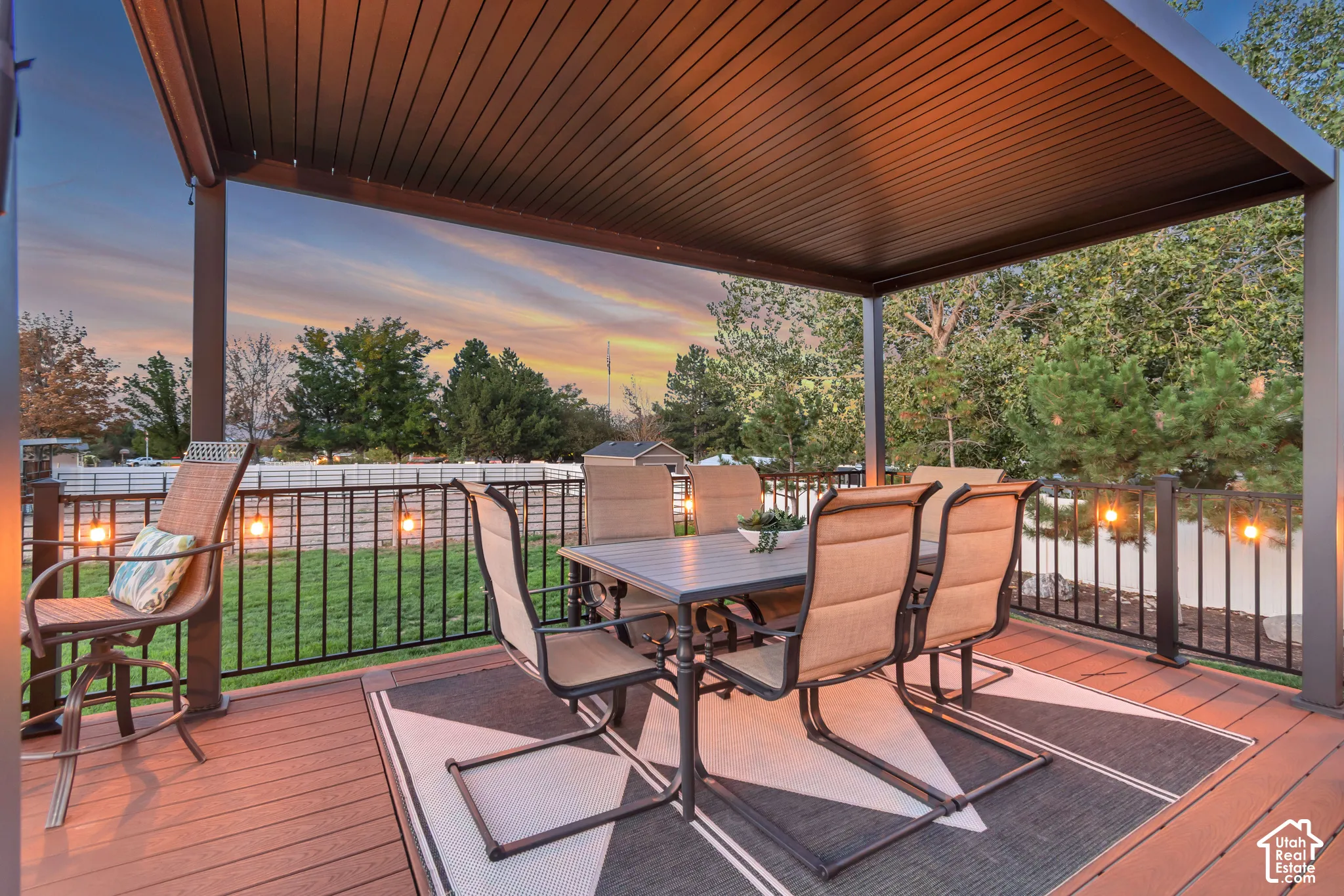 Expansive wood-finish deck with a large black pergola, black metal railing, and string lighting