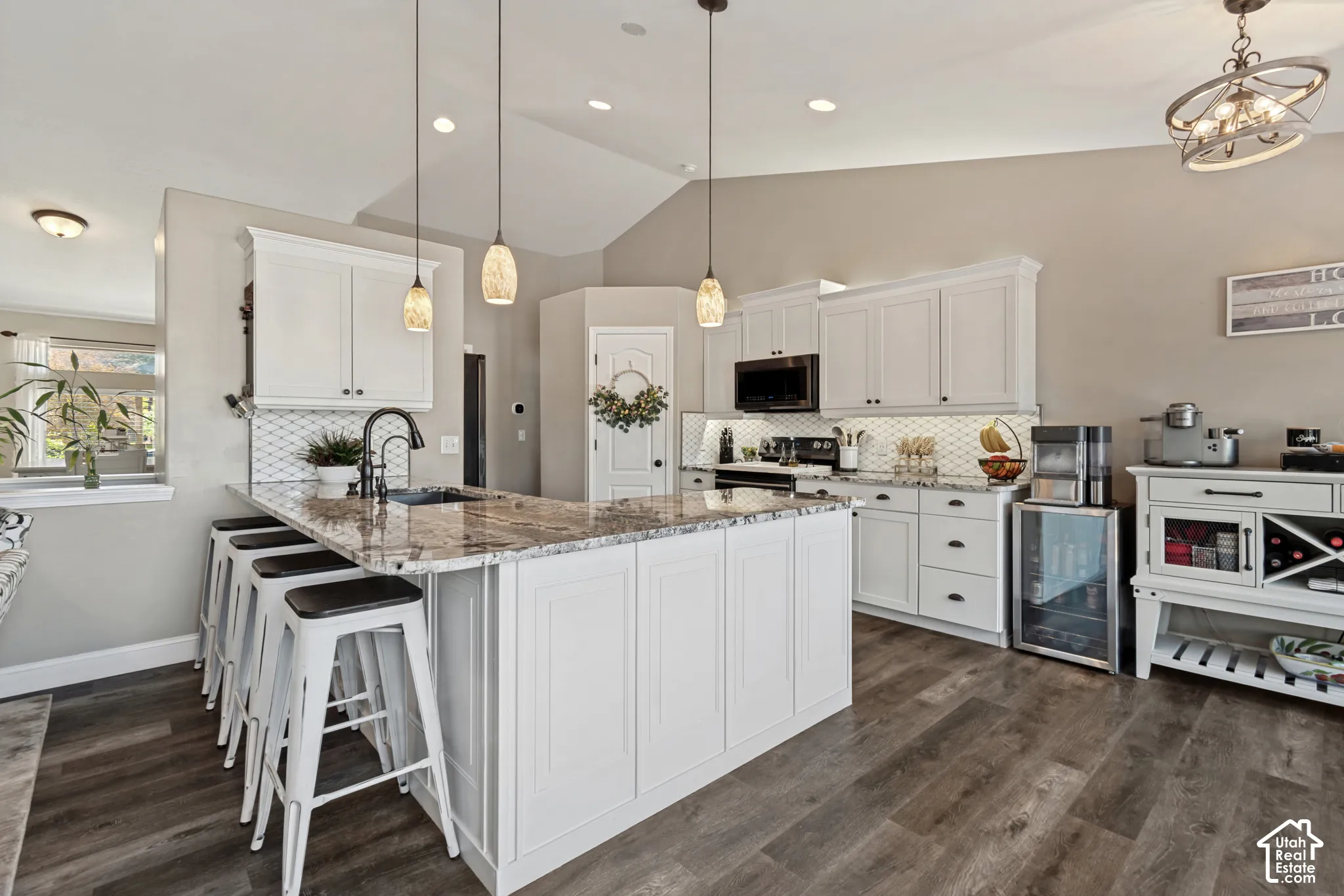 Gourmet kitchen featuring a large central island with seating, white shaker cabinetry, patterned tile backsplash, and wood-finish flooring