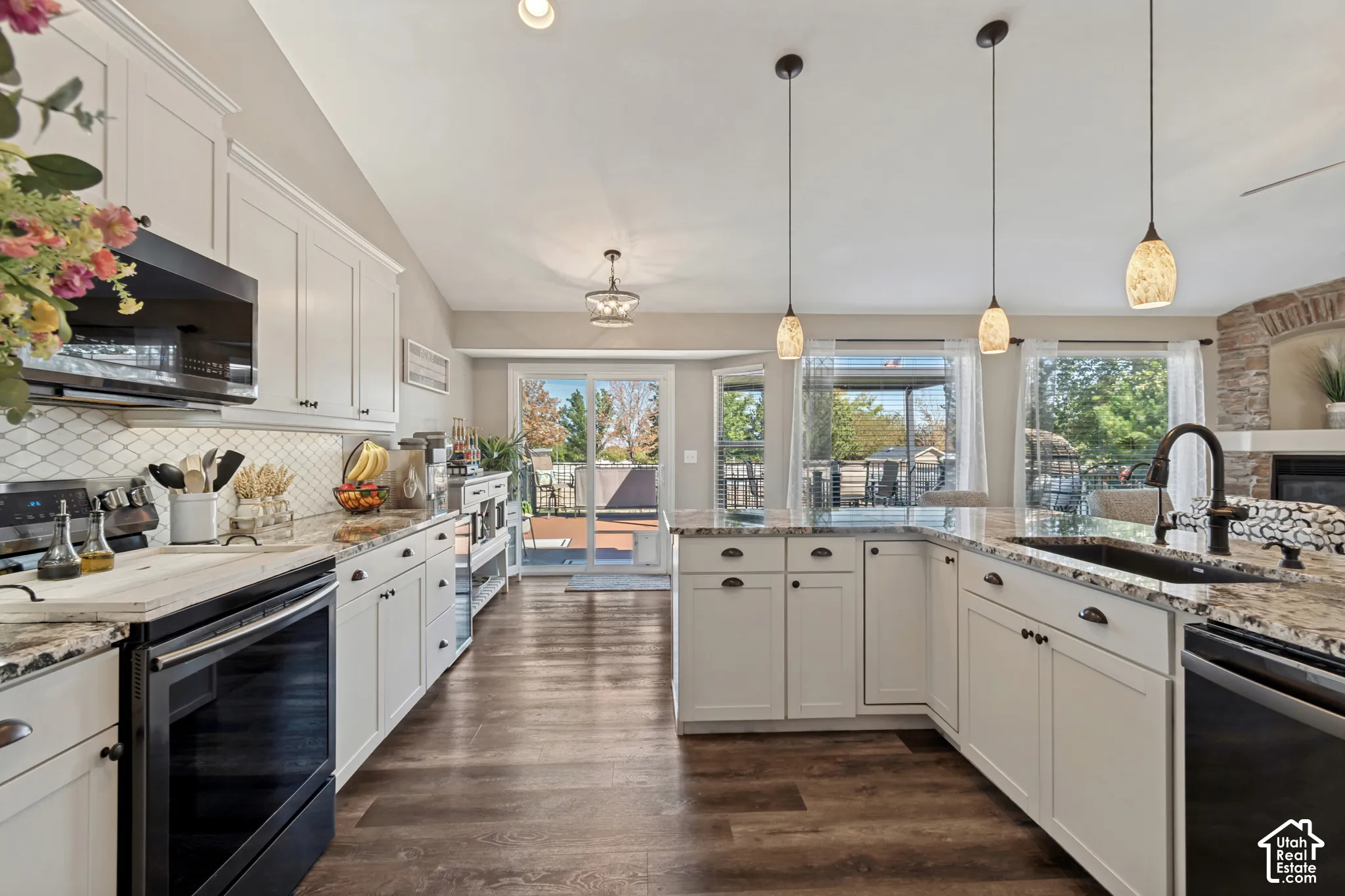 White cabinetry with dark hardware, granite countertops, wood-finish flooring, a tile backsplash, and stainless steel appliances