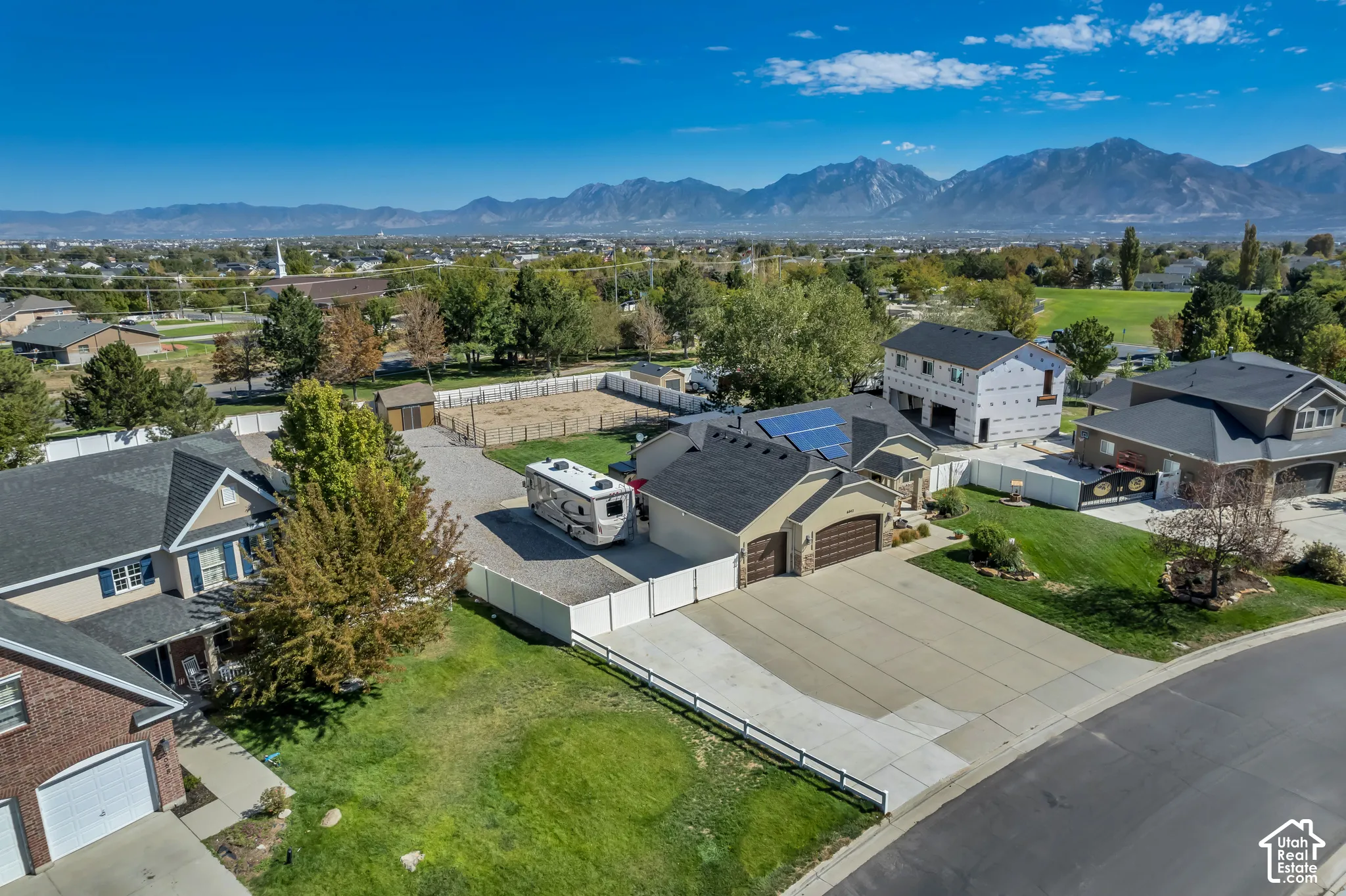Paved driveway, attached garage, solar panel installation, mountain backdrop, and expansive paved area