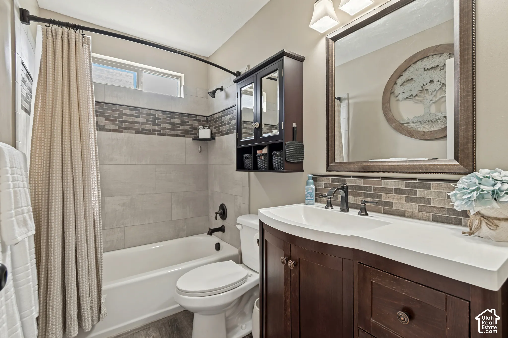 Bathroom featuring a dark wood-finish vanity with an integrated white sink, a framed mirror, and a tiled backsplash