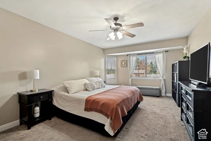 Carpeted flooring, ceiling fan with integrated lighting, multiple windows with blinds and curtain rods, and neutral wall tones