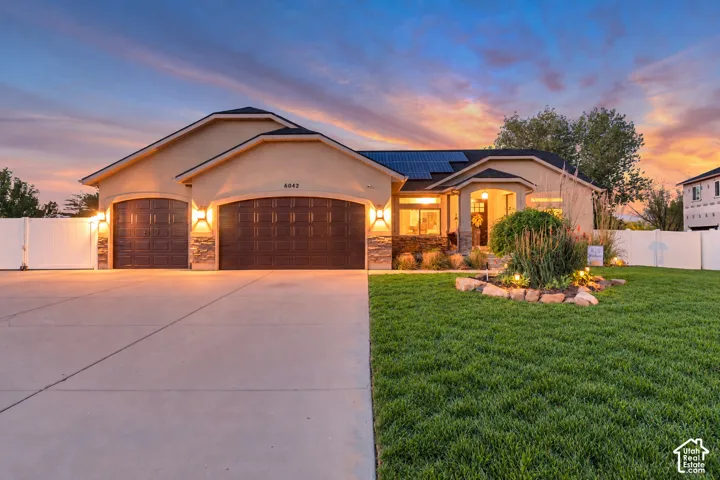 Stucco exterior with stone accents, two-car garage with arched doors, mature landscaping, and a well-maintained lawn