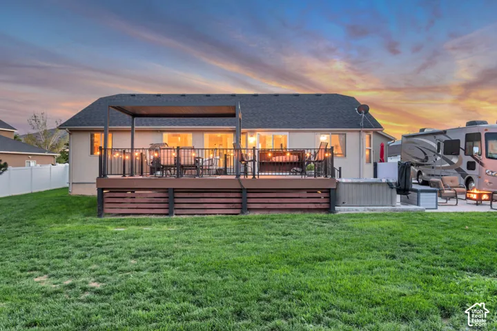Expansive backyard featuring a manicured lawn, a raised wood-finish deck with a pergola, and a paved patio area