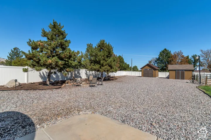Expansive gravel yard featuring mature trees, a white perimeter fence, and two detached storage sheds
