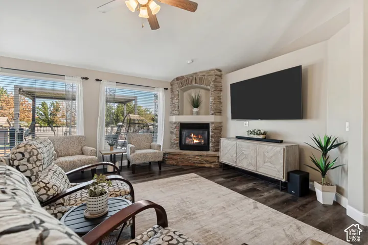 Stone-clad corner fireplace with an arched alcove, dark wood-finish flooring, and multiple windows with horizontal blinds