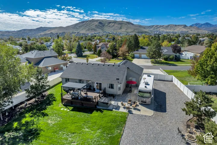 Expansive backyard featuring a manicured lawn, a large deck with a pergola, and a gravel parking area