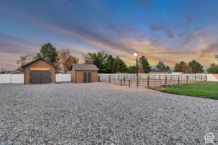 Expansive gravel area with two storage sheds, a white privacy fence, and a metal-fenced enclosure