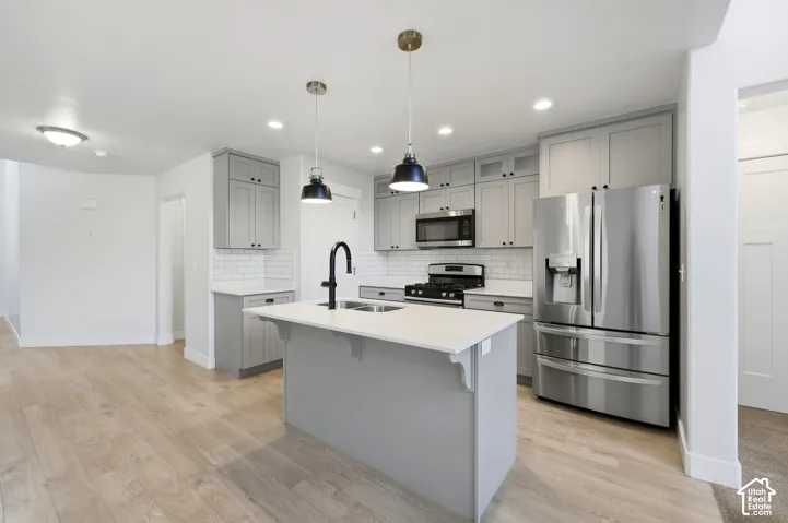 Kitchen featuring stainless steel appliances, a center island with a white countertop, subway tile backsplash, gray cabinetry, and wood-finish flooring