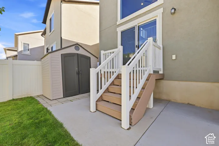 Outdoor patio featuring concrete paving, wooden steps with white railings, a sliding glass door, and a permanent storage shed