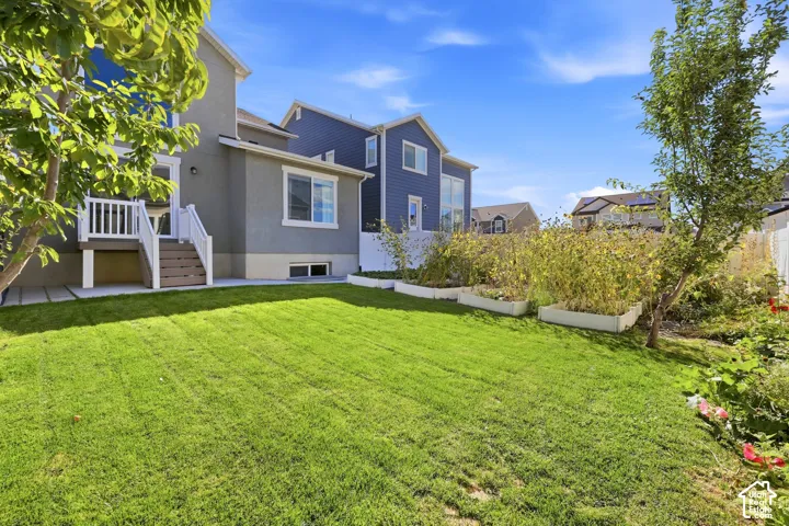 Expansive green lawn, raised garden beds, a privacy fence, and a multi-level exterior with a deck