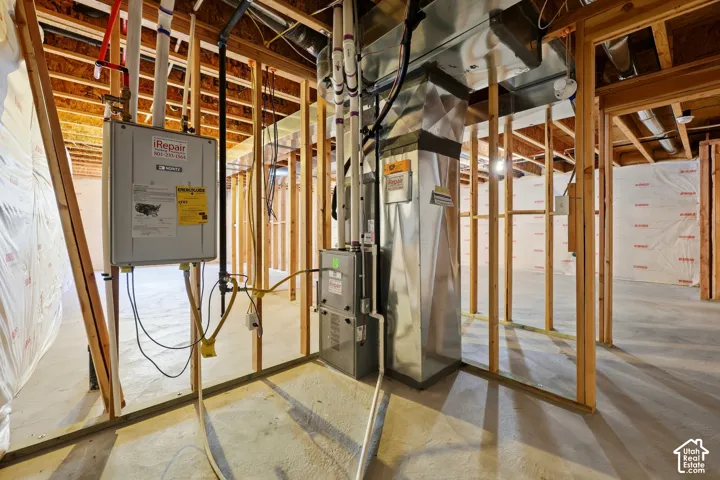 Unfinished basement space featuring exposed wood framing, concrete flooring, a tankless water heater, and HVAC ductwork